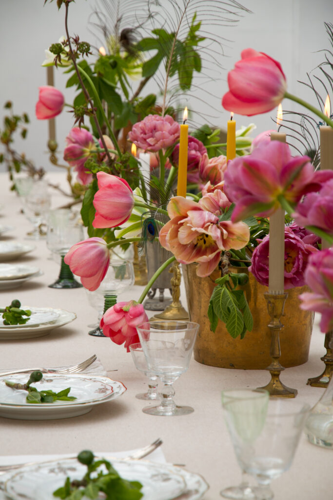 Massor av tulpaner i rosa på ett dukat bord med tända ljus och vintageporslin.