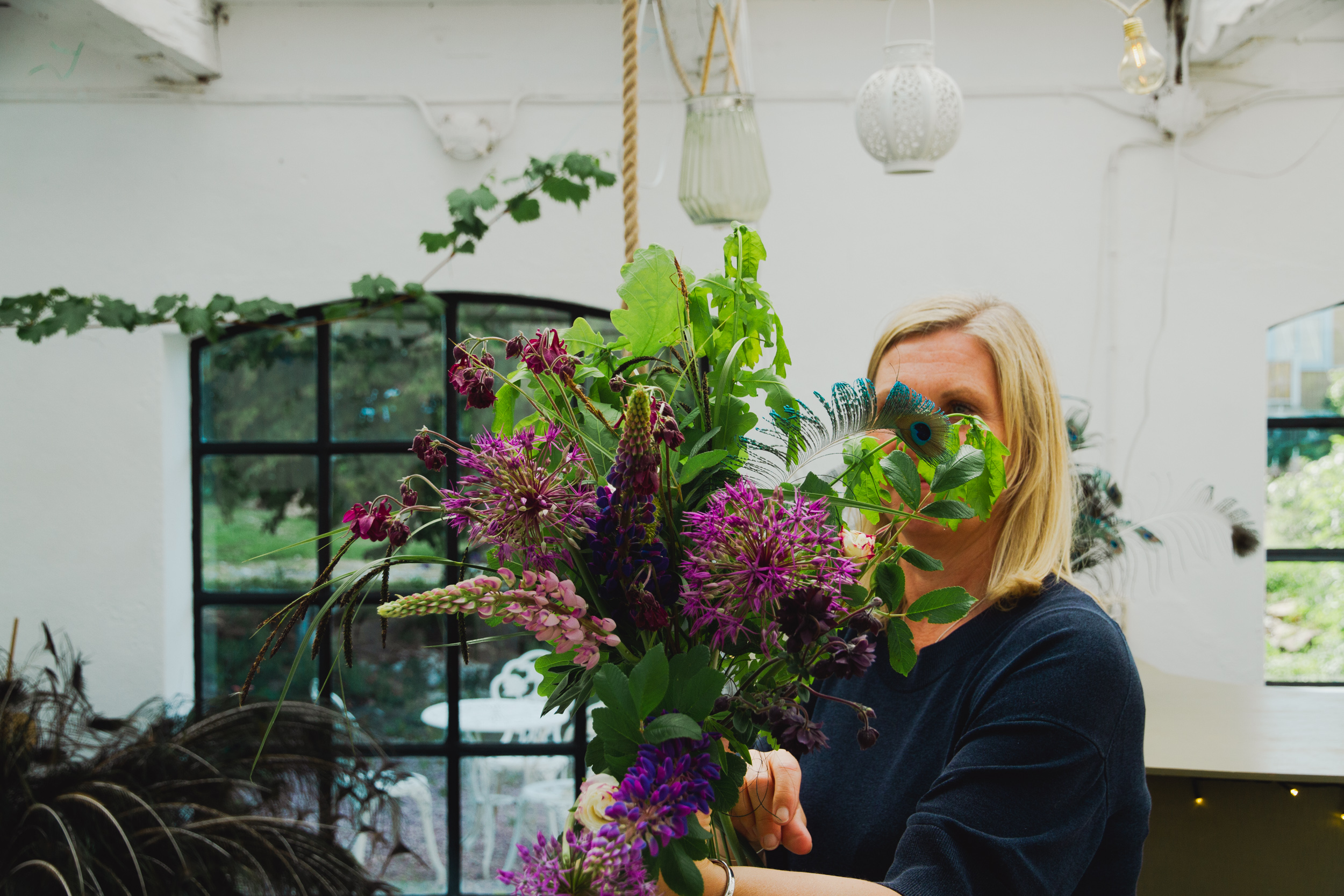 en kvinna med en bukett i handen. Vild och naturlig med allium, lupiner, akleja och påfågelfjädrar.