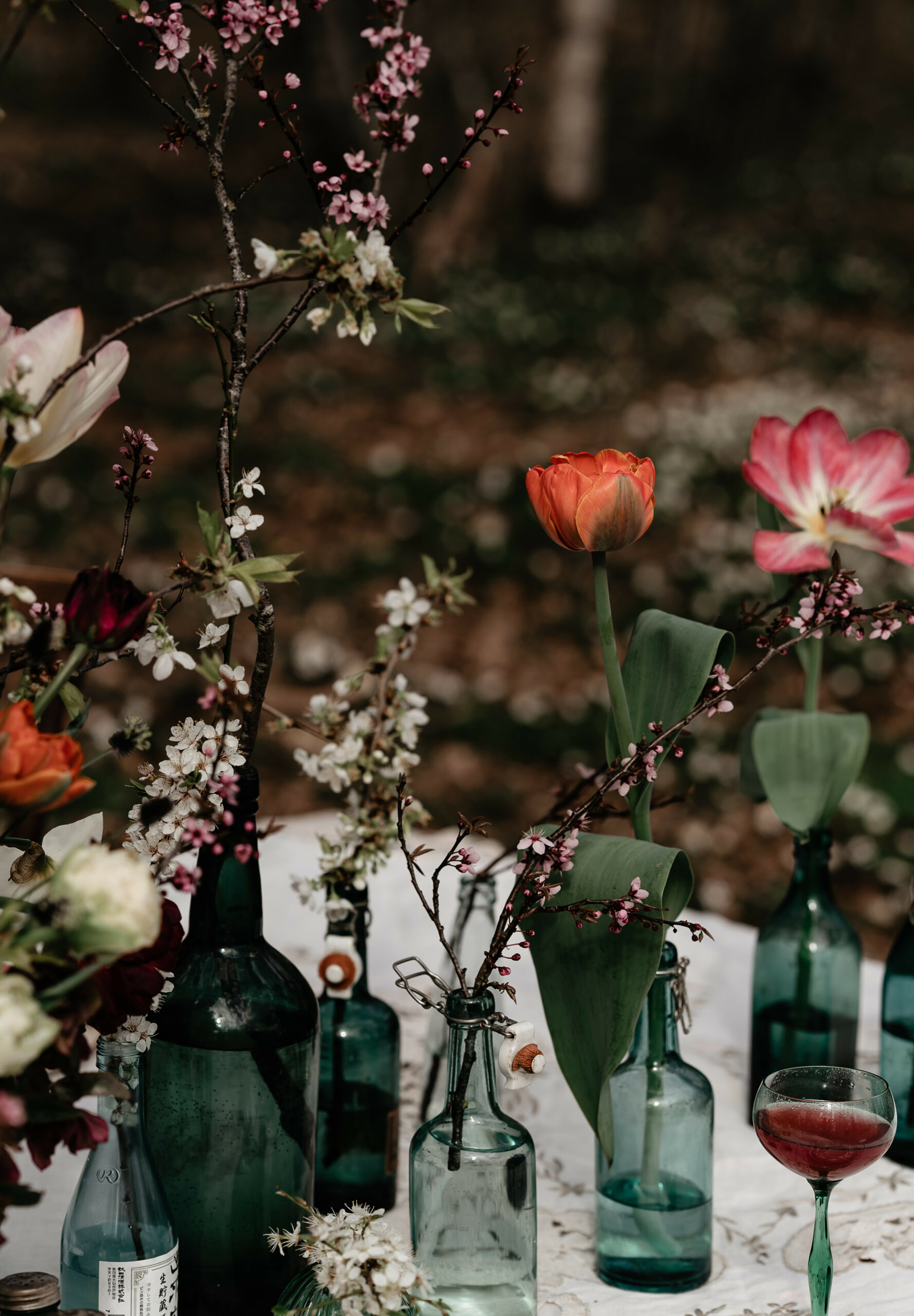 ett dukat bord med blommande kvistar och tulpaner i gröna flaskor.