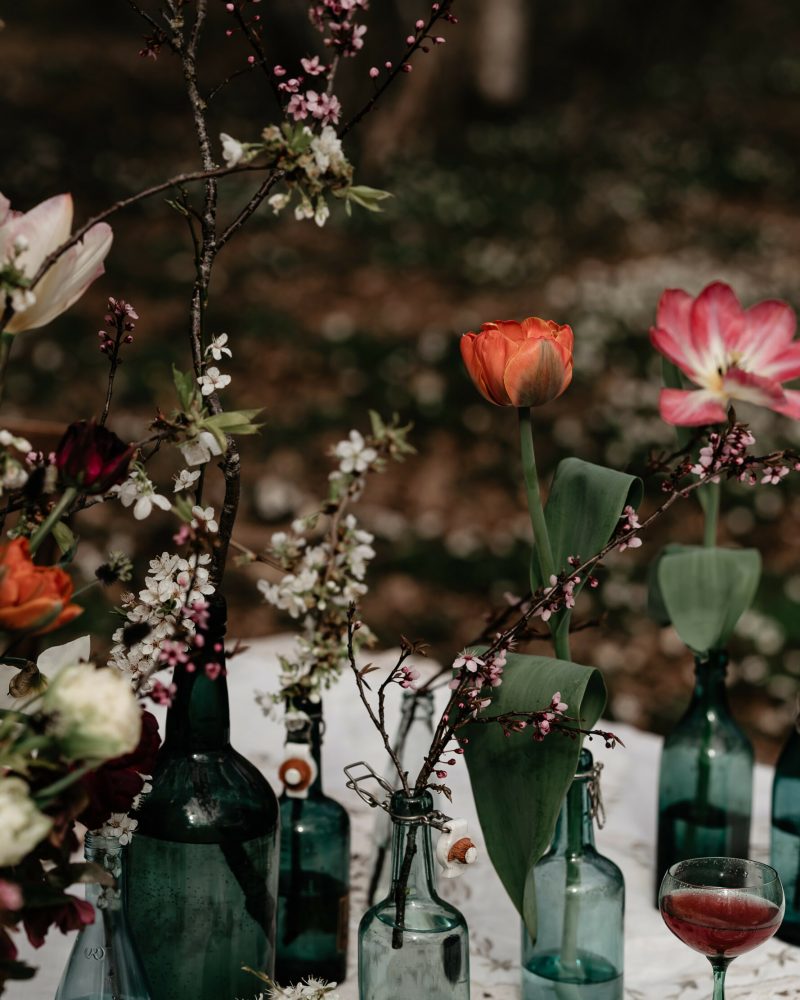 ett dukat bord med blommande kvistar och tulpaner i gröna flaskor.
